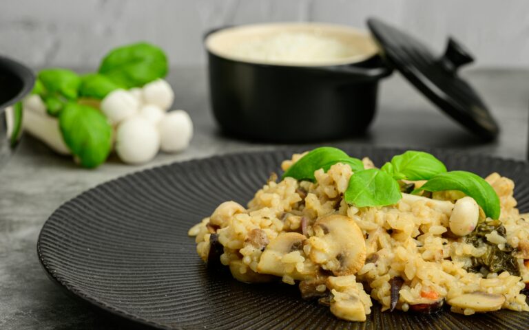 Chestnut Mushroom Risotto with Thyme and Parmesan. Close-up of creamy mushroom risotto topped with basil on a black plate, perfect for foodies.