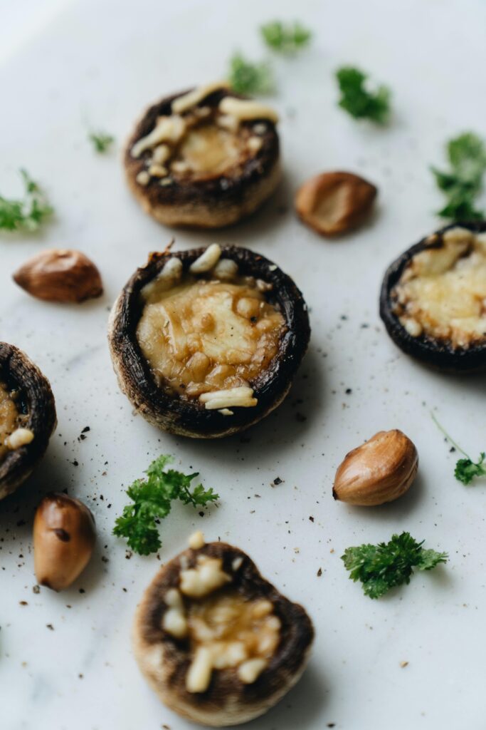 Cheesy Garlic Stuffed Shiitake Mushroom caps close-up of baked mushrooms with cheese, almonds, and fresh parsley on a white surface.