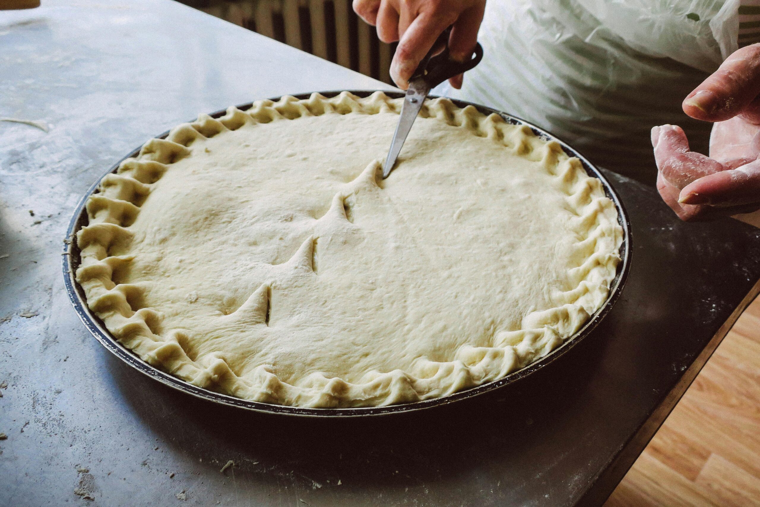 Italian Oyster Mushroom Pot Pie. Hands skillfully trimming homemade pie crust with scissors in a kitchen setting.